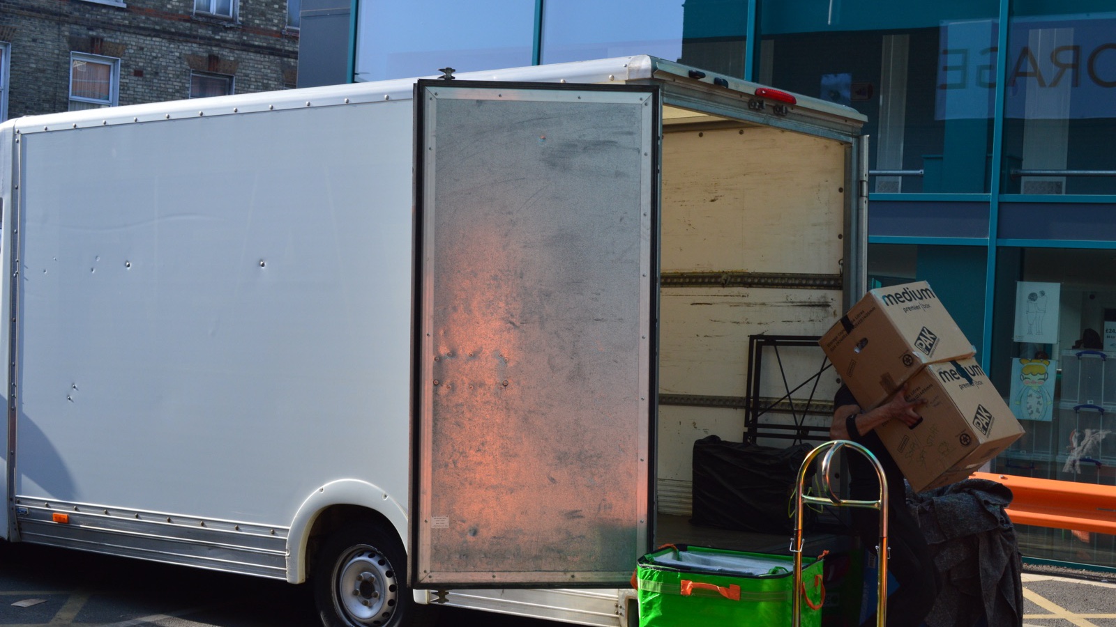 Removal worker carrying stacked boxes beside an open unbranded Luton vehicle