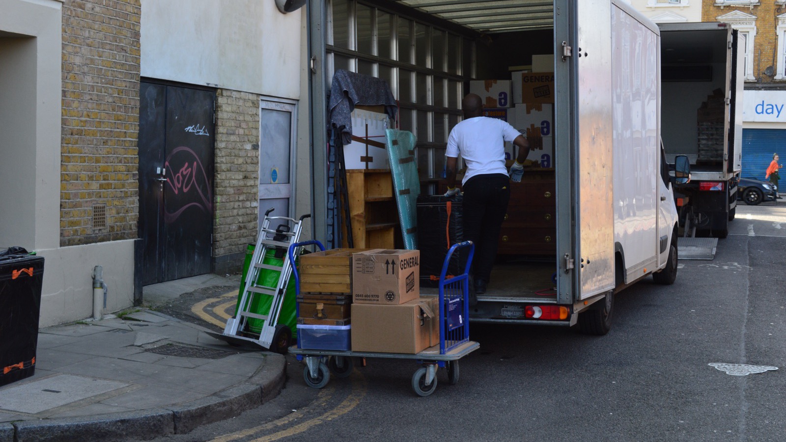 Removal worker loading furniture into a Luton van on a narrow London street