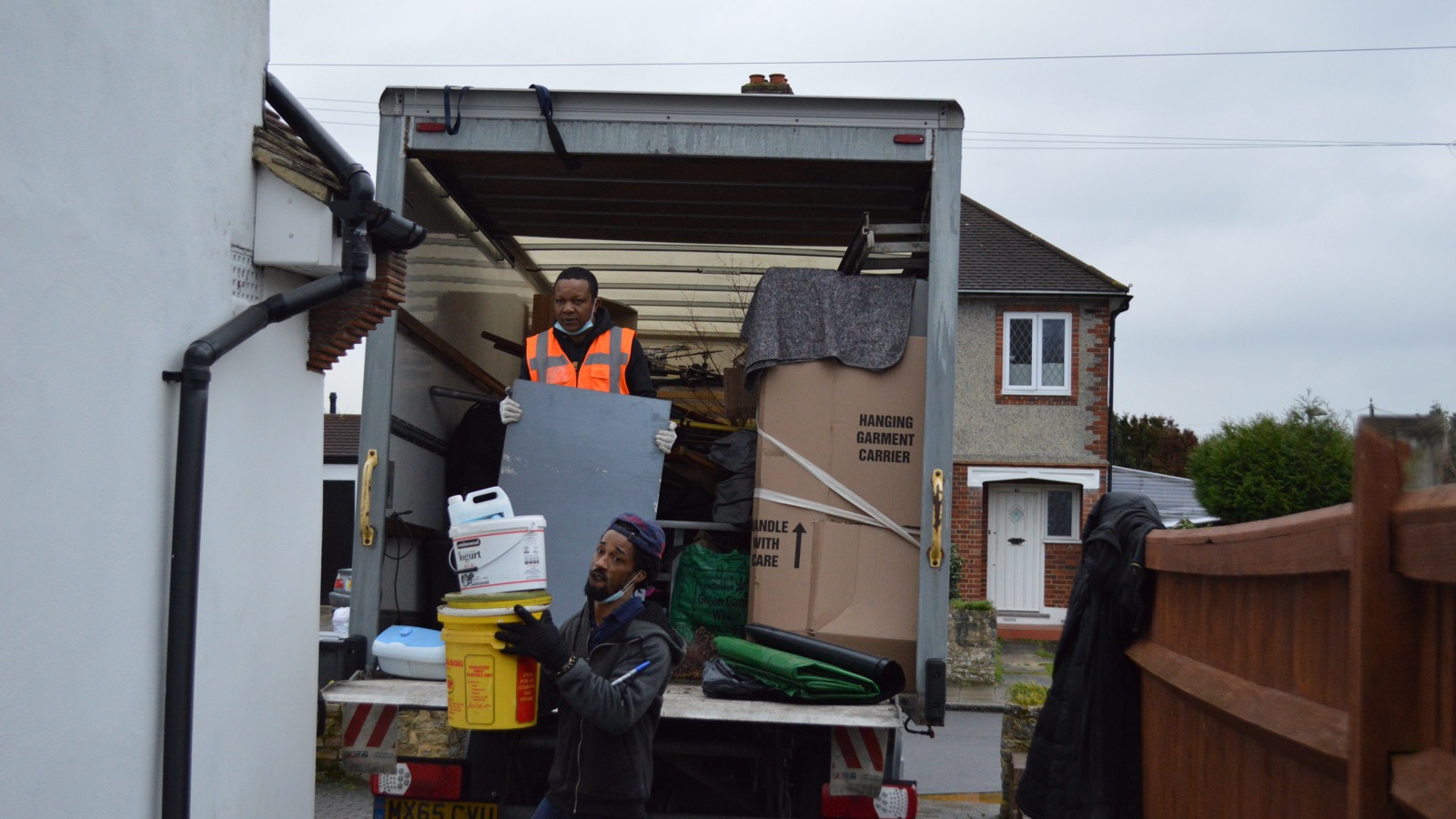 Two removal workers handling household items at the rear of an unbranded Luton vehicle