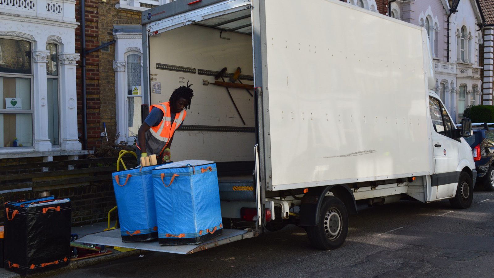 A real removal worker loading blue household bags at the rear of an unbranded Luton vehicle