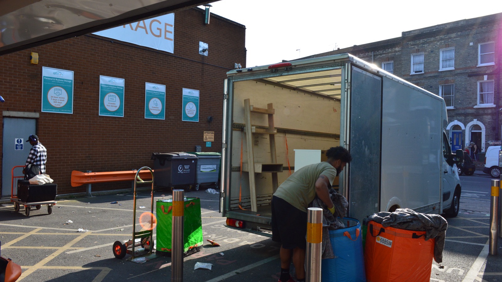 Removal worker loading household goods into an open Luton van outside a storage facility