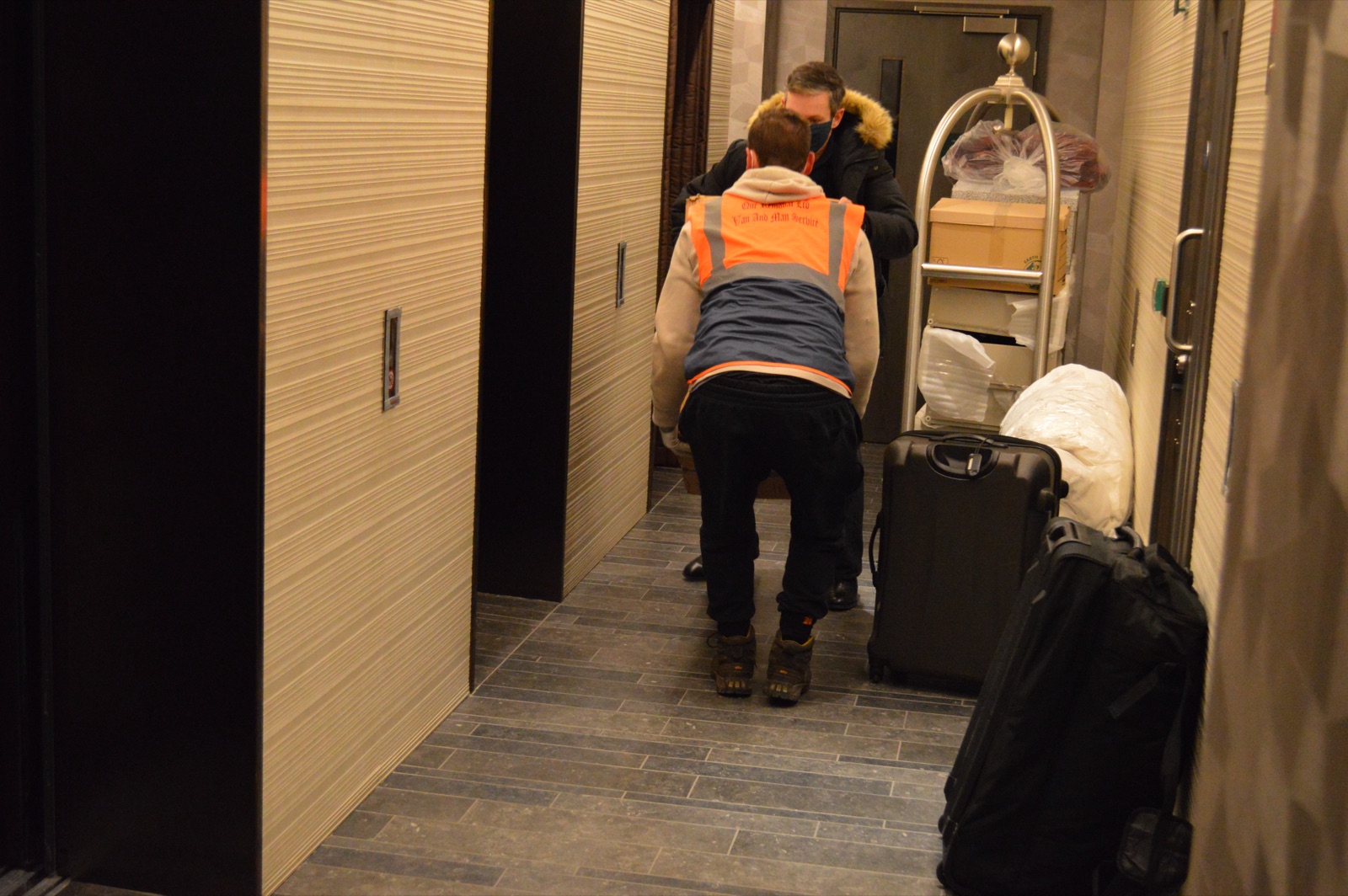 Mover handling an apartment corridor move with luggage and boxes